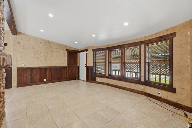 2875 North Hill Field Road, Unit 111 Layton, UT 84041 - Photo 10 of 30 Empty room featuring wallpapered walls, a wainscoted wall, vaulted ceiling, wood walls, and light tile patterned flooring