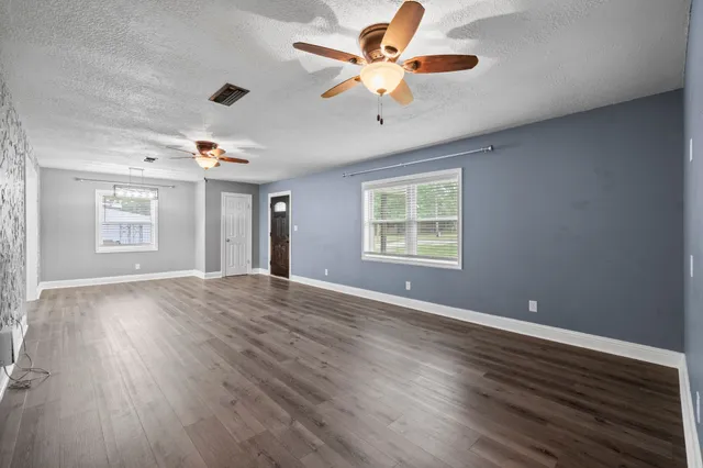 an empty room with wooden floor chandelier fan and windows