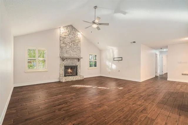 an empty room with wooden floor fireplace and windows