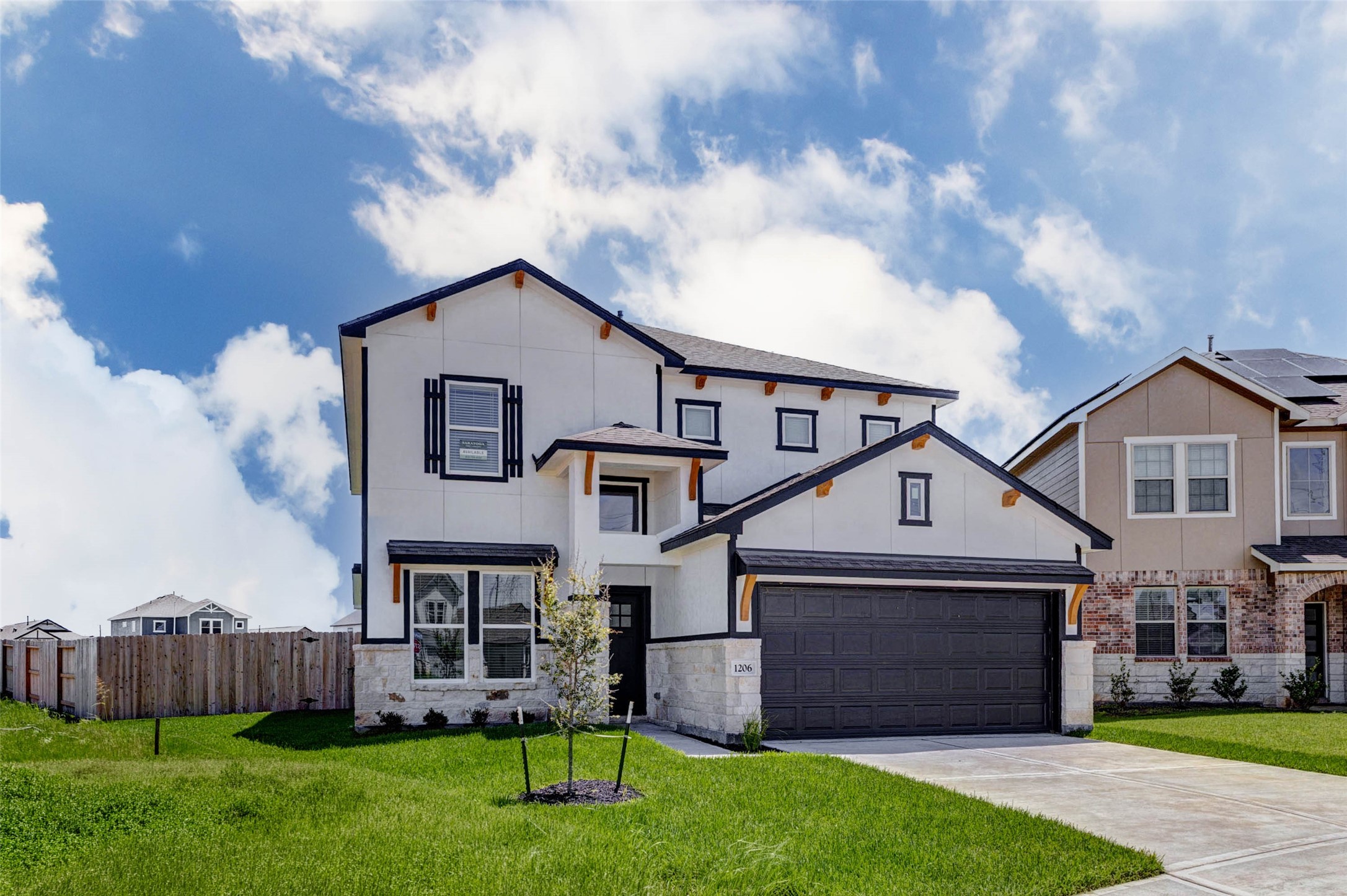 Beautiful front elevation with standout curb appeal, featuring a two-story design, black-framed windows, stone accents, decorative wood brackets, and a welcoming covered entry. The oversized driveway leads to an attached two-car garage, while the front lawn and young landscaping add a polished touch. The side fencing enhances privacy and hints at the spacious backyard beyond.