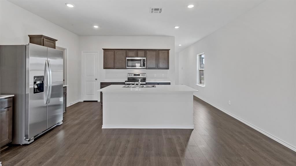 212 Pheasant Run Road Terrell, TX 75160 - Photo 14 of 24 Kitchen featuring dark wood-finish cabinetry, stainless steel appliances, a center island with sink, white countertops, and wood-finish flooring