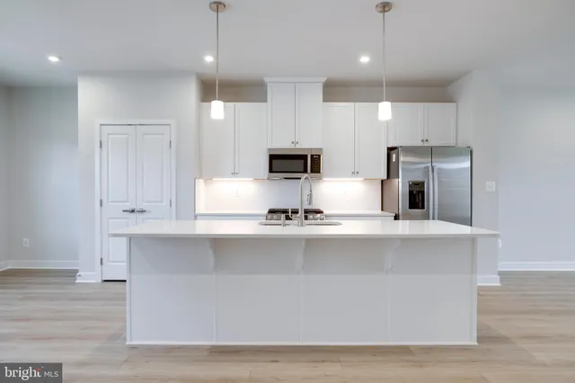 a large kitchen with granite countertop a stove a sink a refrigerator and white cabinets with wooden floor