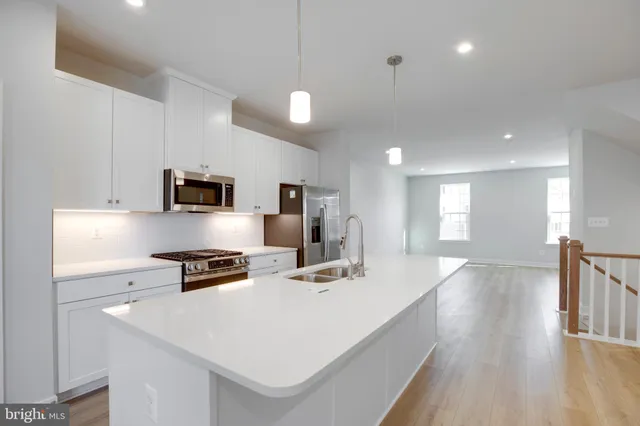 a kitchen with stainless steel appliances a sink a stove a microwave a refrigerator a white counter and cabinets