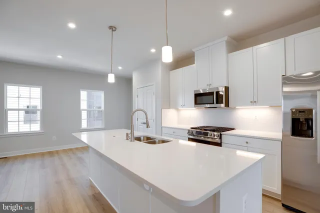 a kitchen with stainless steel appliances granite countertop a sink a stove a refrigerator and white cabinets with wooden floor