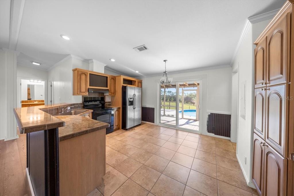 17355 Southeast 260th Avenue Road Umatilla, FL 32784 - Photo 14 of 69 a large kitchen with kitchen island granite countertop a refrigerator a stove top oven a sink a dining table and chairs with wooden floor