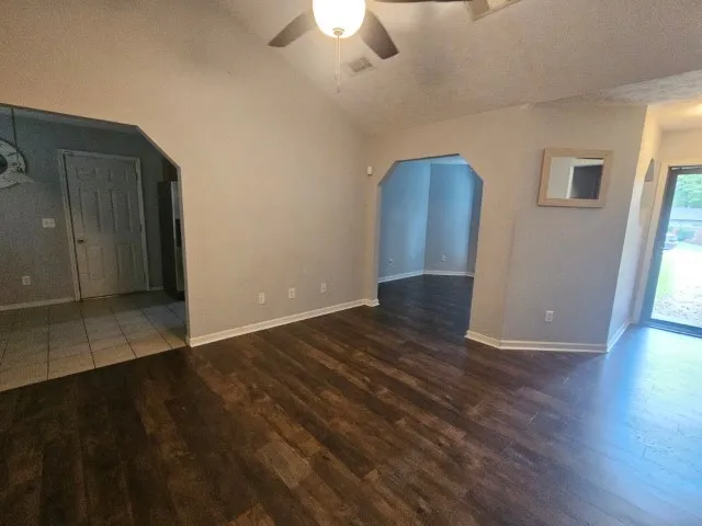 an empty room with wooden floor chandelier fan and windows