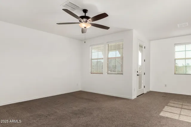 an empty room with chandelier fan and windows
