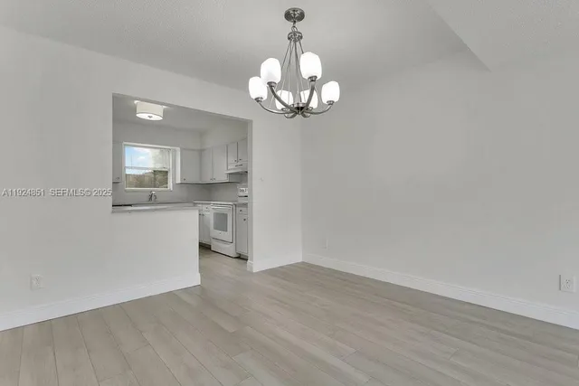a view of an empty room with wooden floor and a kitchen