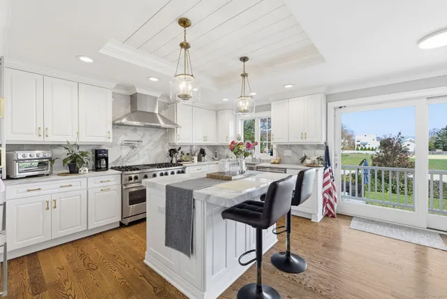 a kitchen with stainless steel appliances kitchen island granite countertop a stove a sink a refrigerator and white cabinets with wooden floor