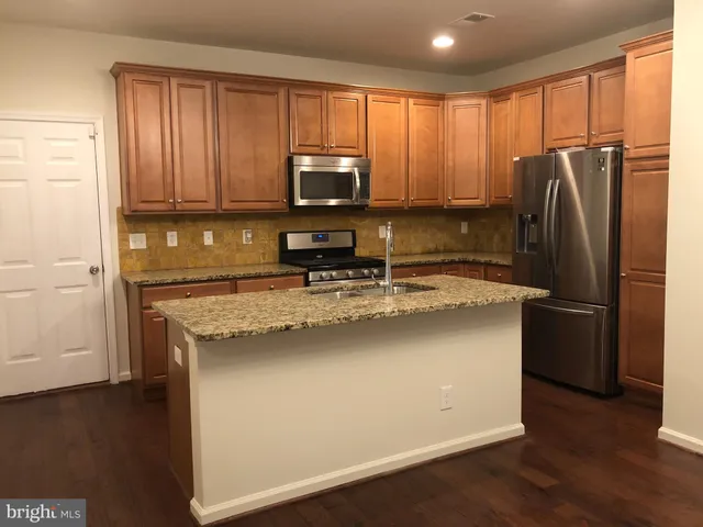 a kitchen with stainless steel appliances granite countertop a refrigerator a stove a sink and a microwave with wooden floor