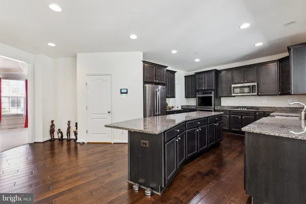 a kitchen with stainless steel appliances granite countertop a stove top oven a sink a refrigerator white cabinets and wooden floor