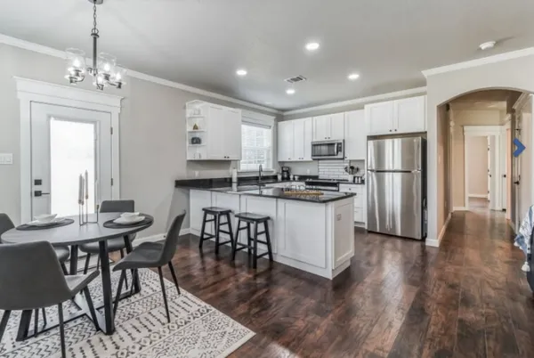 a kitchen with stainless steel appliances kitchen island granite countertop a dining table chairs refrigerator and sink