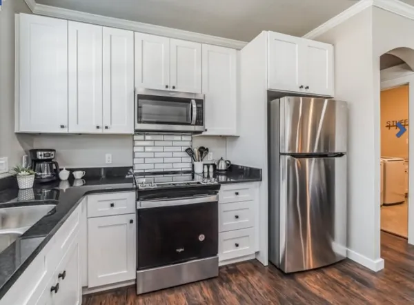 a kitchen with granite countertop a refrigerator stove and sink with wooden floor