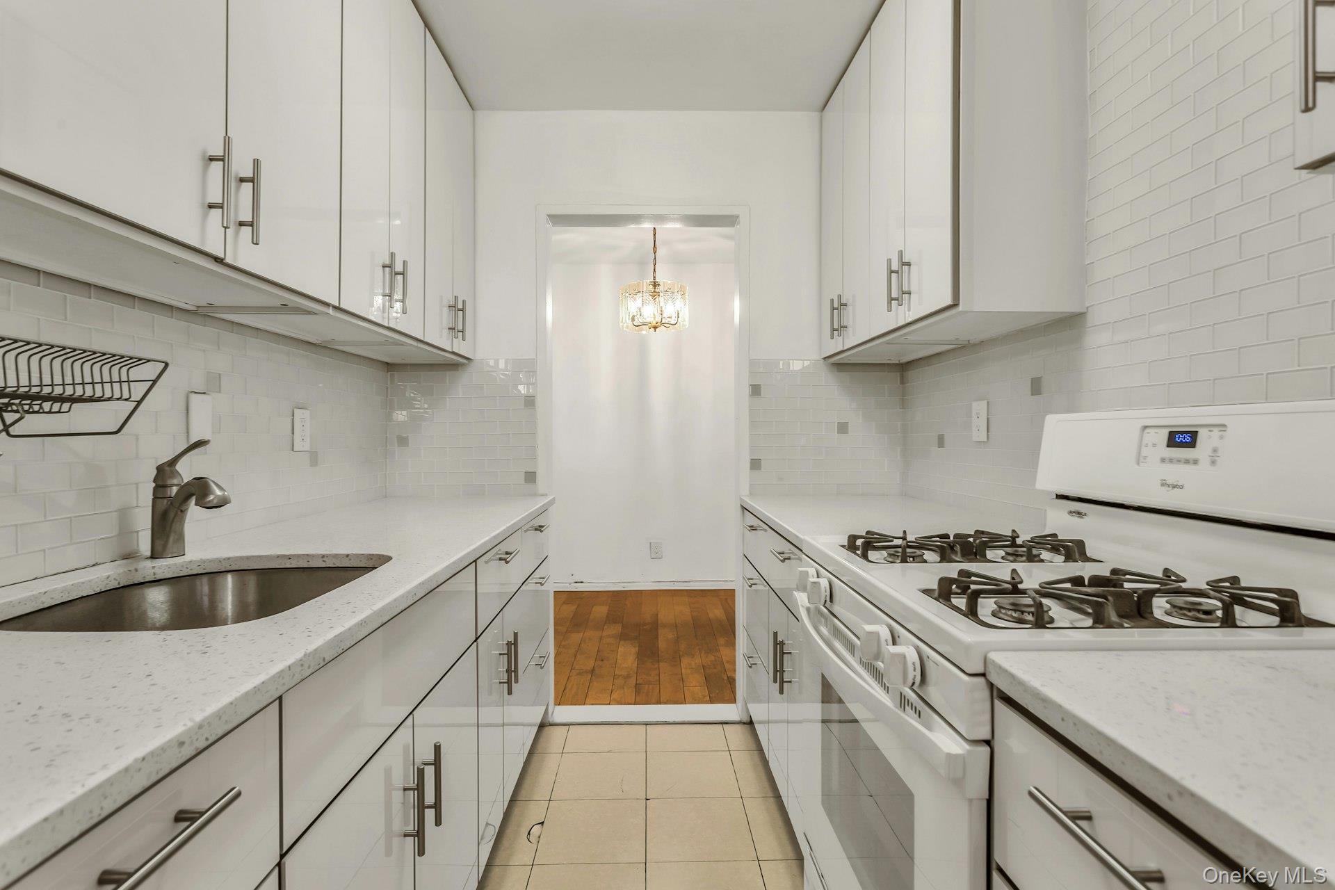 138-10 Franklin Avenue, Unit 9J Queens, NY 11355 - Photo 13 of 25 Kitchen with white gas range oven, light stone countertops, light tile patterned floors, white cabinetry, and a chandelier