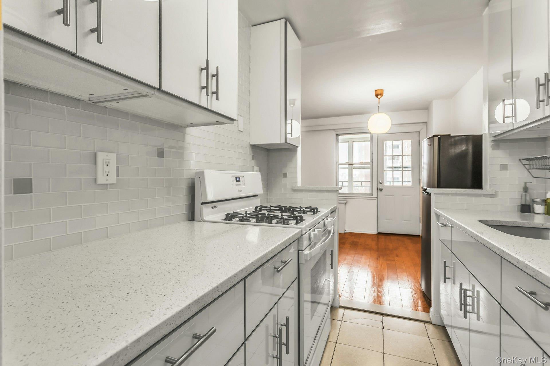 138-10 Franklin Avenue, Unit 9J Queens, NY 11355 - Photo 14 of 25 Kitchen featuring white gas stove, freestanding refrigerator, light stone countertops, pendant lighting, and backsplash