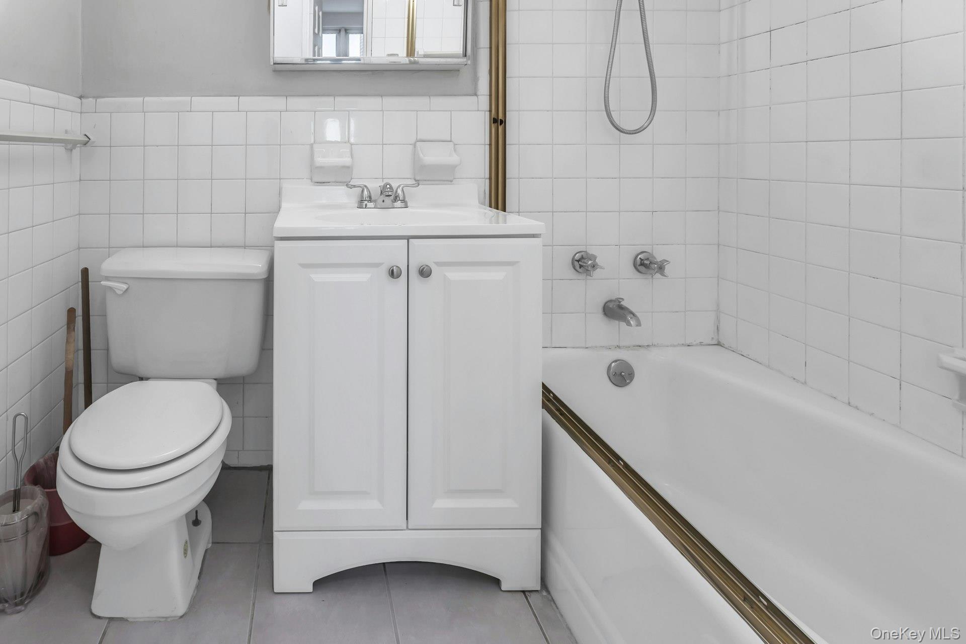 138-10 Franklin Avenue, Unit 9J Queens, NY 11355 - Photo 20 of 25 Full bathroom with tile walls, bathtub / shower combination, vanity, a wainscoted wall, and light tile patterned floors