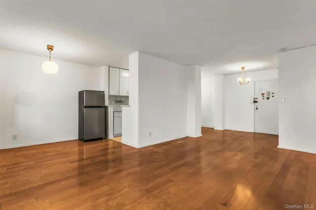 a view of empty room with wooden floor and kitchen
