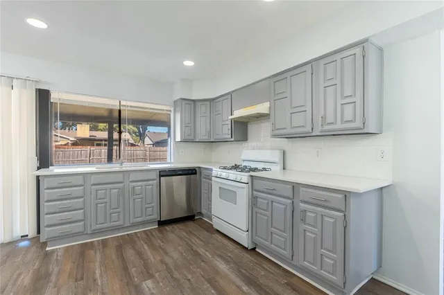 a kitchen with stainless steel appliances granite countertop a stove top oven a sink dishwasher and white cabinets with wooden floor