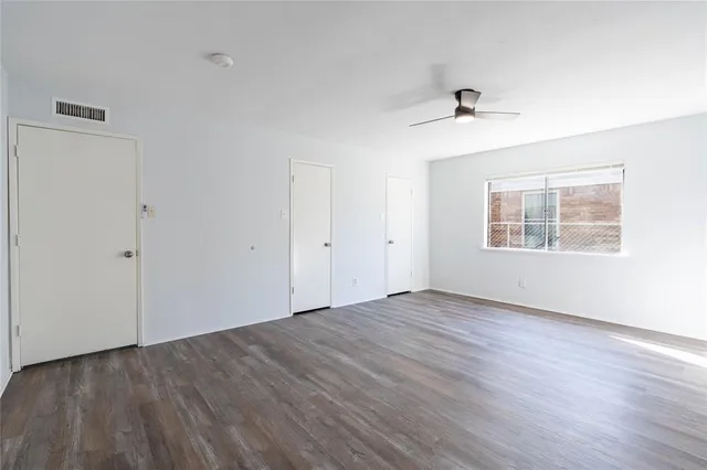 an empty room with wooden floor chandelier fan and windows