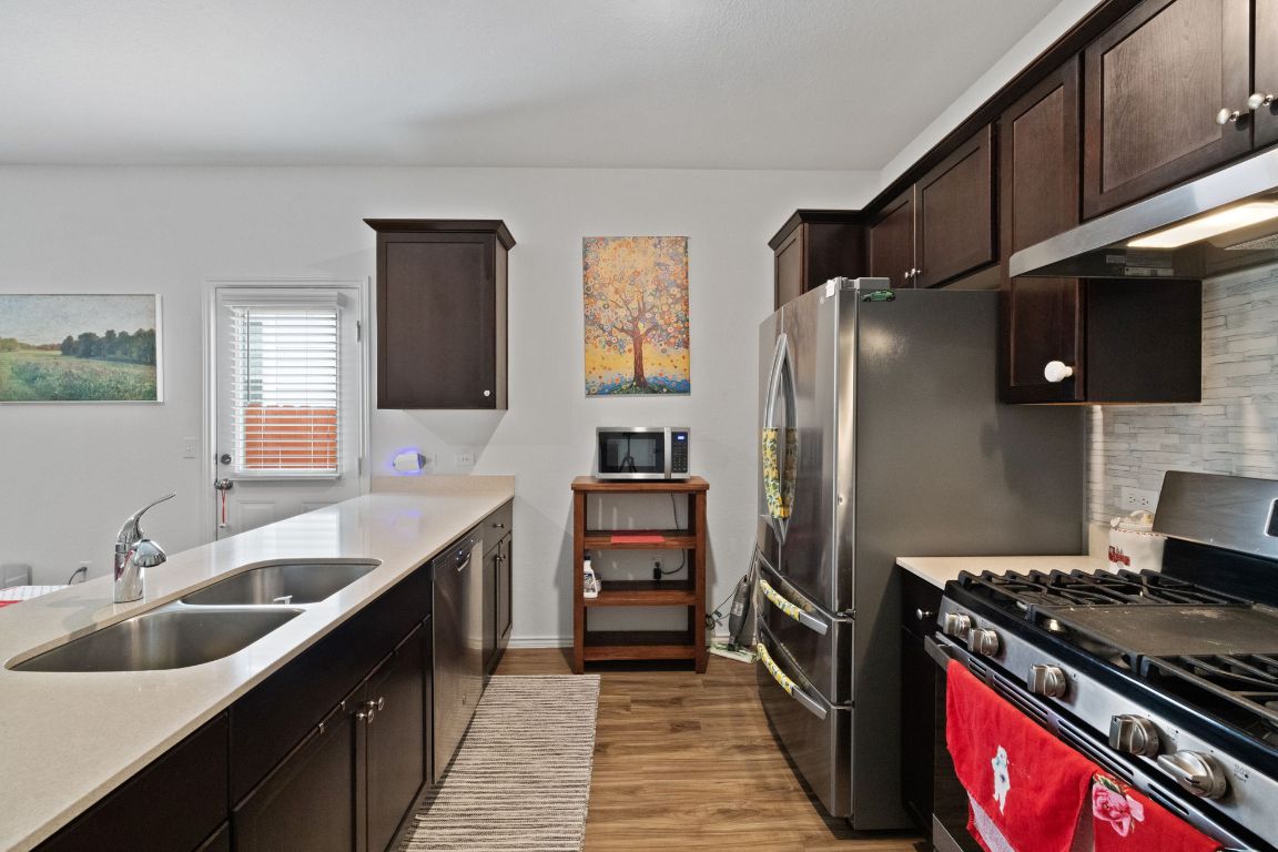 7116 Spirit Hill Road Austin, TX 78744 - Photo 12 of 33 Kitchen featuring appliances with stainless steel finishes, dark brown cabinets, light wood-style flooring, and exhaust hood