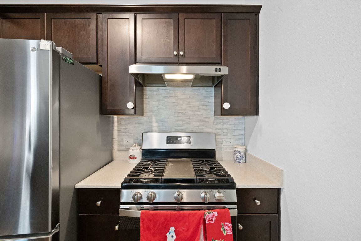 7116 Spirit Hill Road Austin, TX 78744 - Photo 13 of 33 Kitchen featuring appliances with stainless steel finishes, dark brown cabinetry, under cabinet range hood, and backsplash