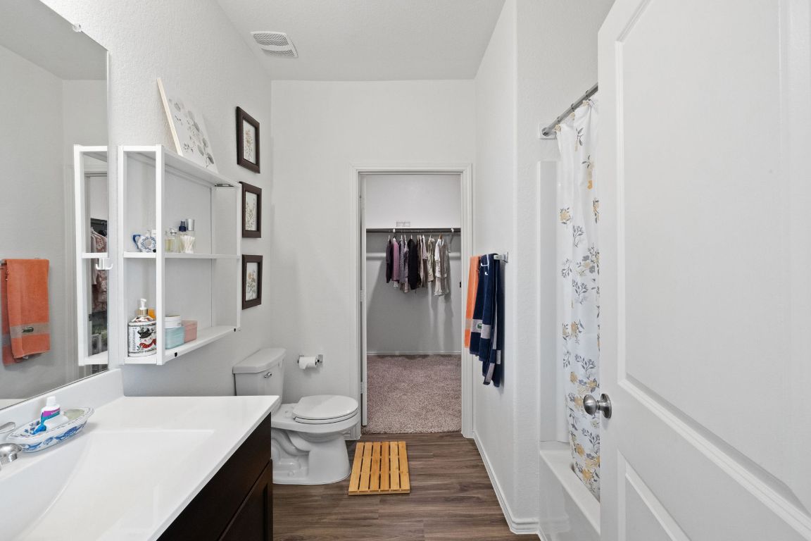 7116 Spirit Hill Road Austin, TX 78744 - Photo 18 of 33 Bathroom with vanity, dark wood-style floors, a walk in closet, and shower / bath combination with curtain