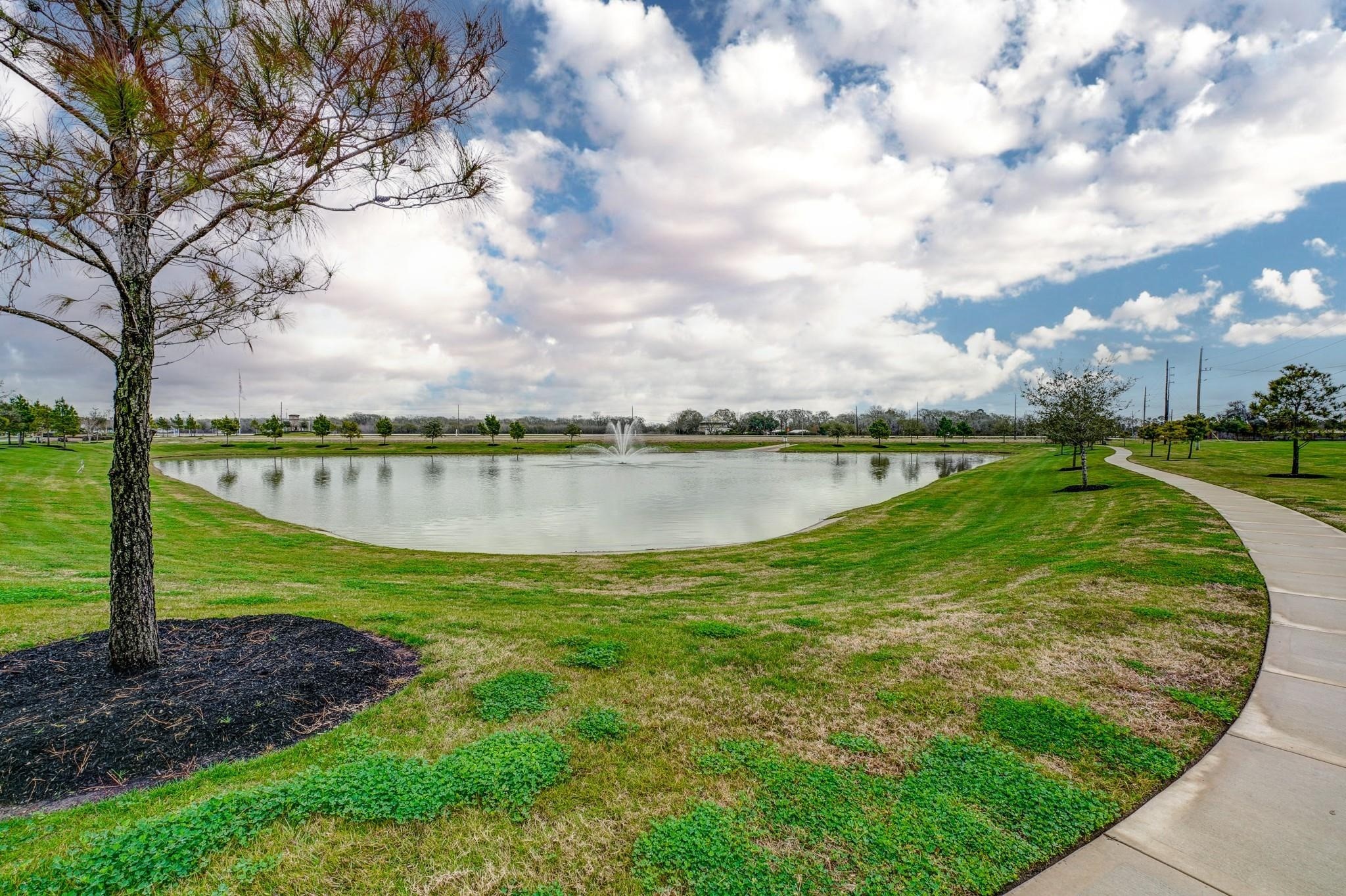 2639 Finley Lane Rosenberg, TX 77471 - Photo 17 of 18 This photo showcases a serene lake with a central fountain, surrounded by well-maintained green lawns and a walking path, perfect for leisurely strolls and outdoor relaxation.