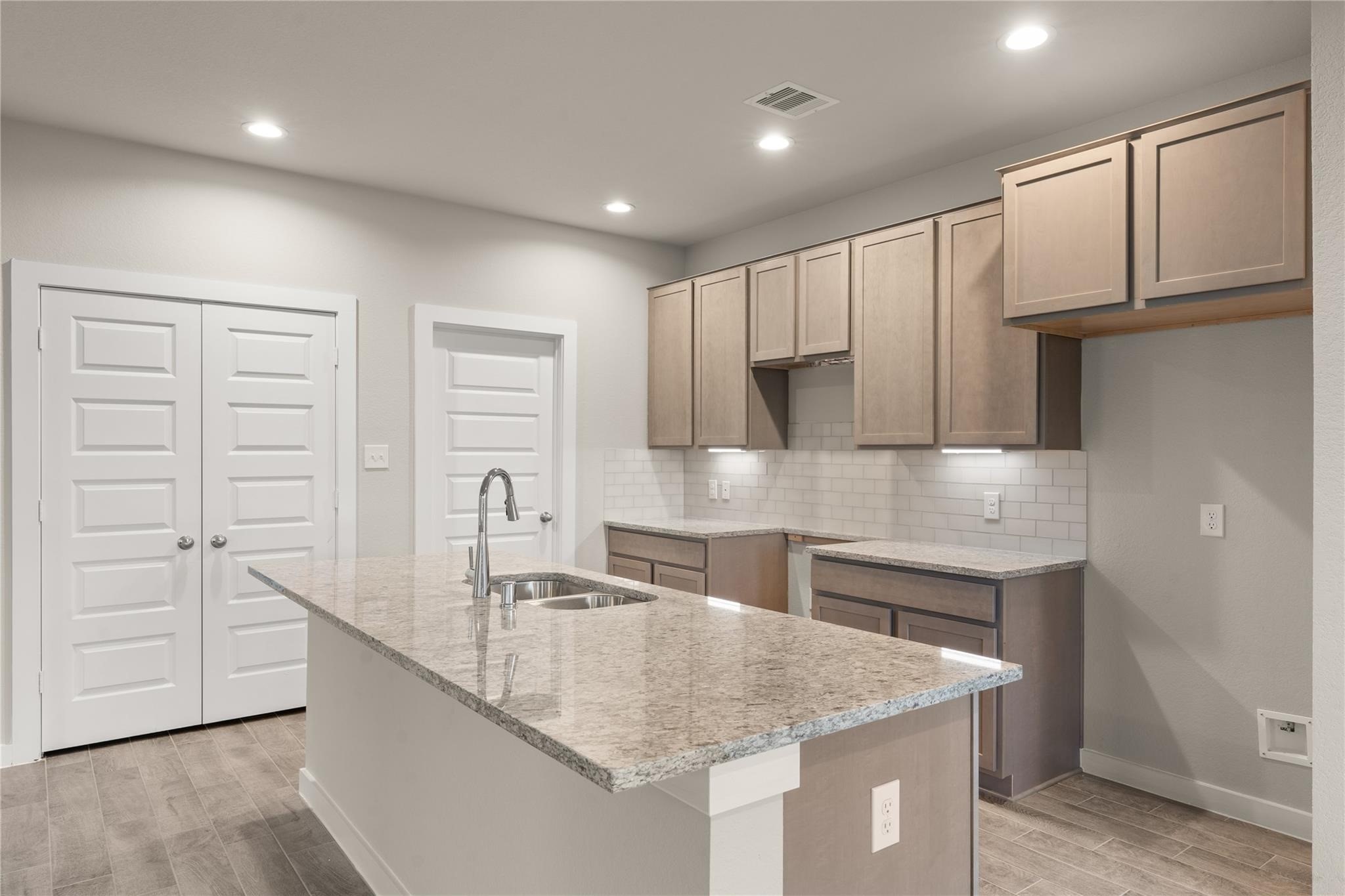 2639 Finley Lane Rosenberg, TX 77471 - Photo 3 of 18 This modern kitchen features sleek granite countertops, ample cabinetry, and a subway tile backsplash. It includes a central island with a built-in sink and stylish fixtures, set against a backdrop of neutral tones and recessed lighting.