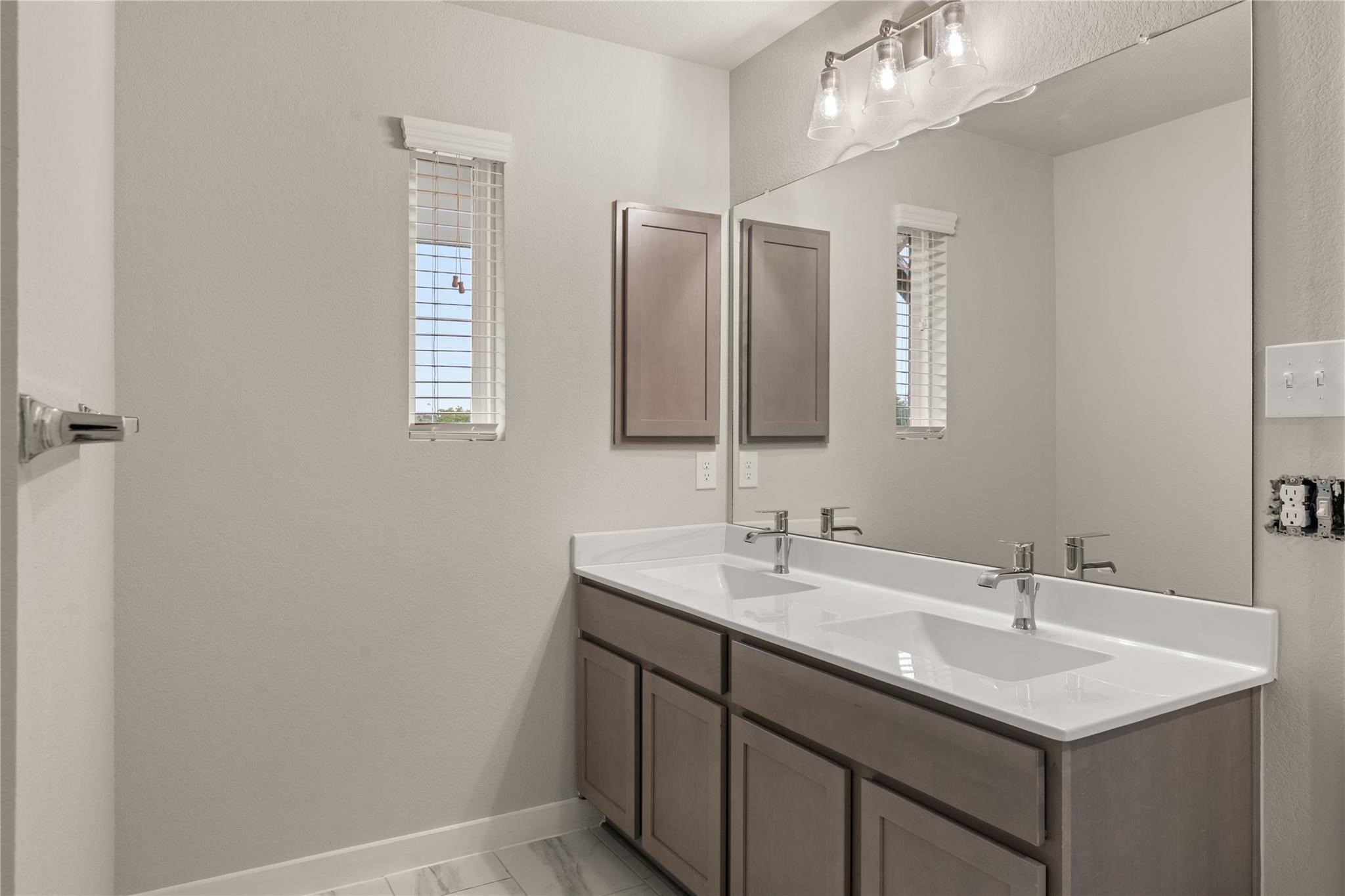 2639 Finley Lane Rosenberg, TX 77471 - Photo 6 of 18 This bathroom features a sleek double vanity with modern fixtures, ample storage, and a large mirror. Two narrow windows provide natural light, complementing the clean and contemporary design.