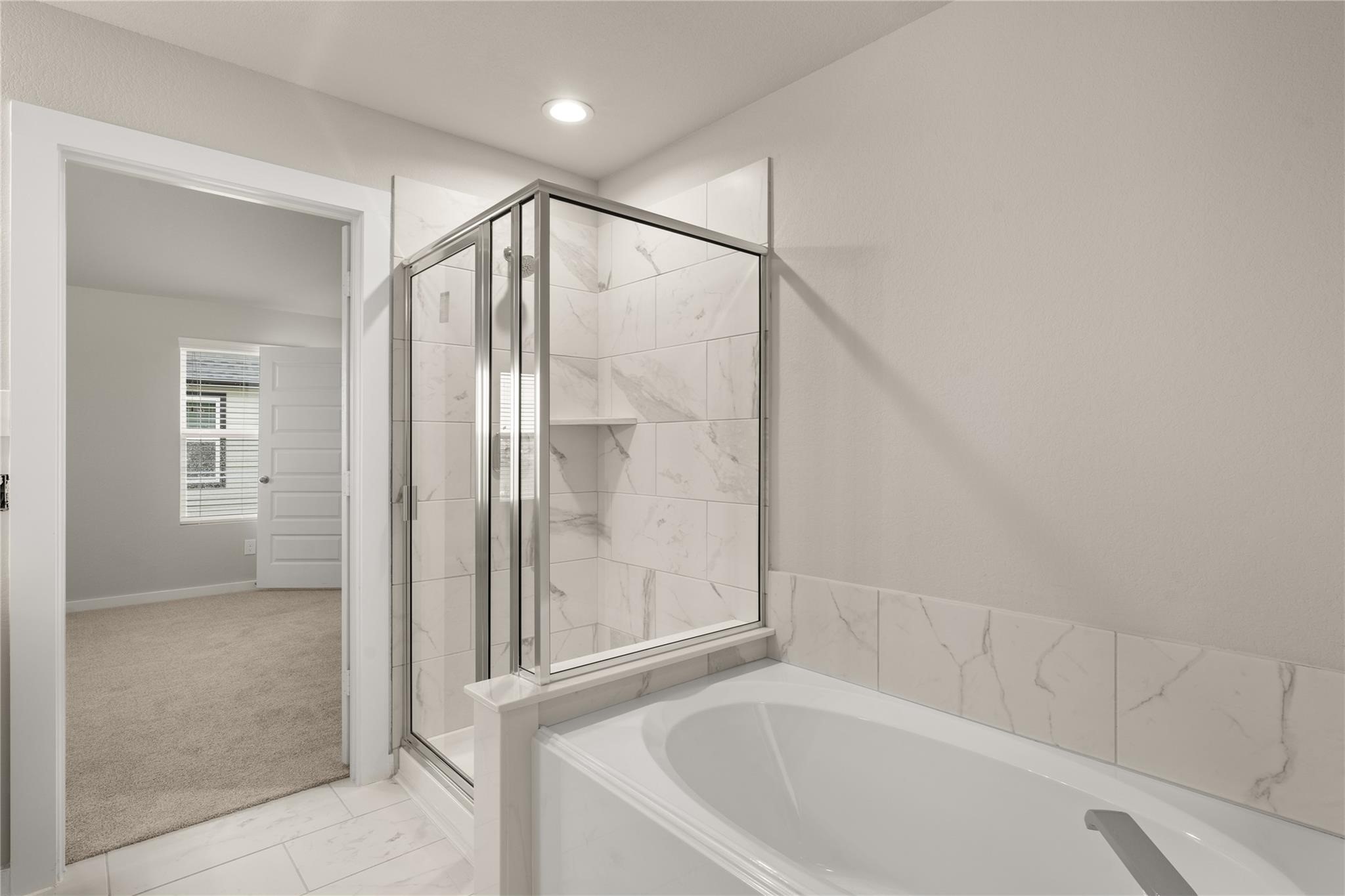 2639 Finley Lane Rosenberg, TX 77471 - Photo 7 of 18 This photo showcases a modern bathroom featuring a glass-enclosed shower and a separate bathtub with elegant marble-like tile. The neutral tones provide a clean, contemporary look, and an adjacent carpeted room is visible through the open door.