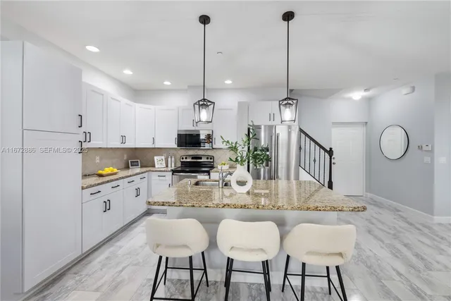a kitchen with stainless steel appliances kitchen island granite countertop a dining table chairs and white cabinets