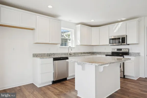 a kitchen with stainless steel appliances granite countertop a sink a stove a microwave a refrigerator a white cabinets and wooden floor