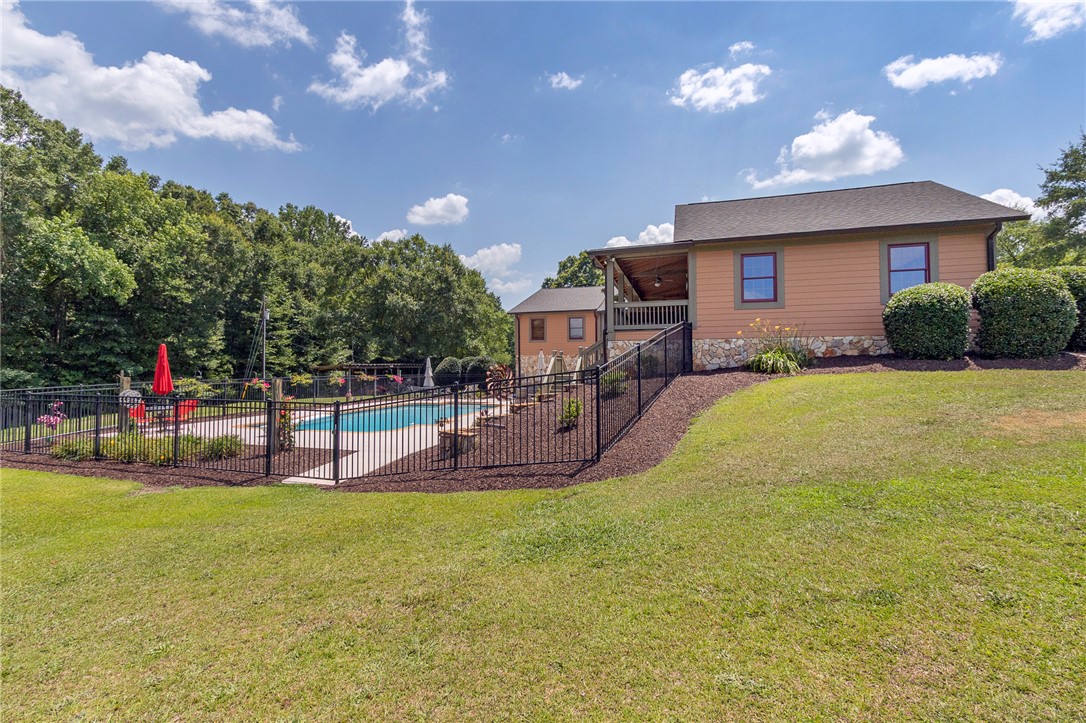 911 State Rd S-4-203 Belton, SC 29627 - Photo 45 of 49 An inviting backyard oasis features a fenced-in swimming pool alongside a covered porch and manicured landscaping.
