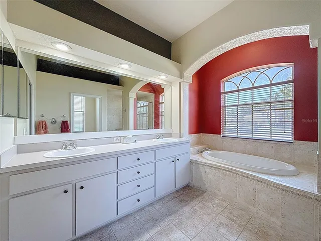 a spacious bathroom with a double vanity sink a large mirror a bathtub and next to a window