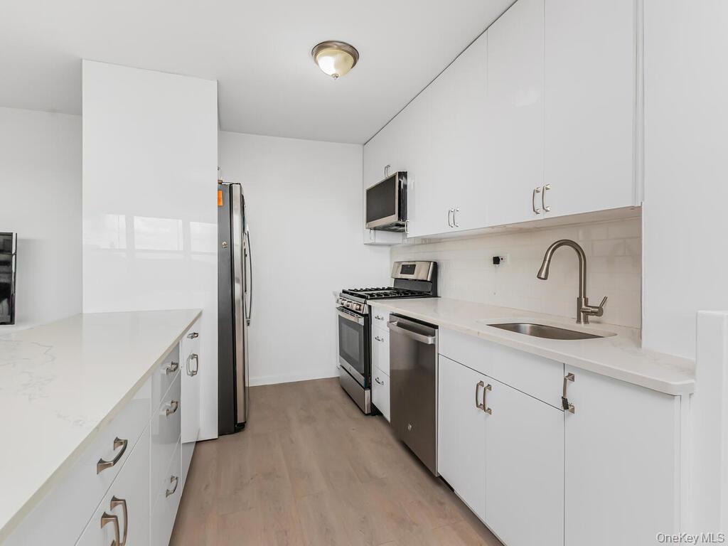 555 Kappock Street, Unit 16K Bronx, NY 10463 - Photo 8 of 16 Kitchen with appliances with stainless steel finishes, a sink, backsplash, light wood-style floors, and white cabinets