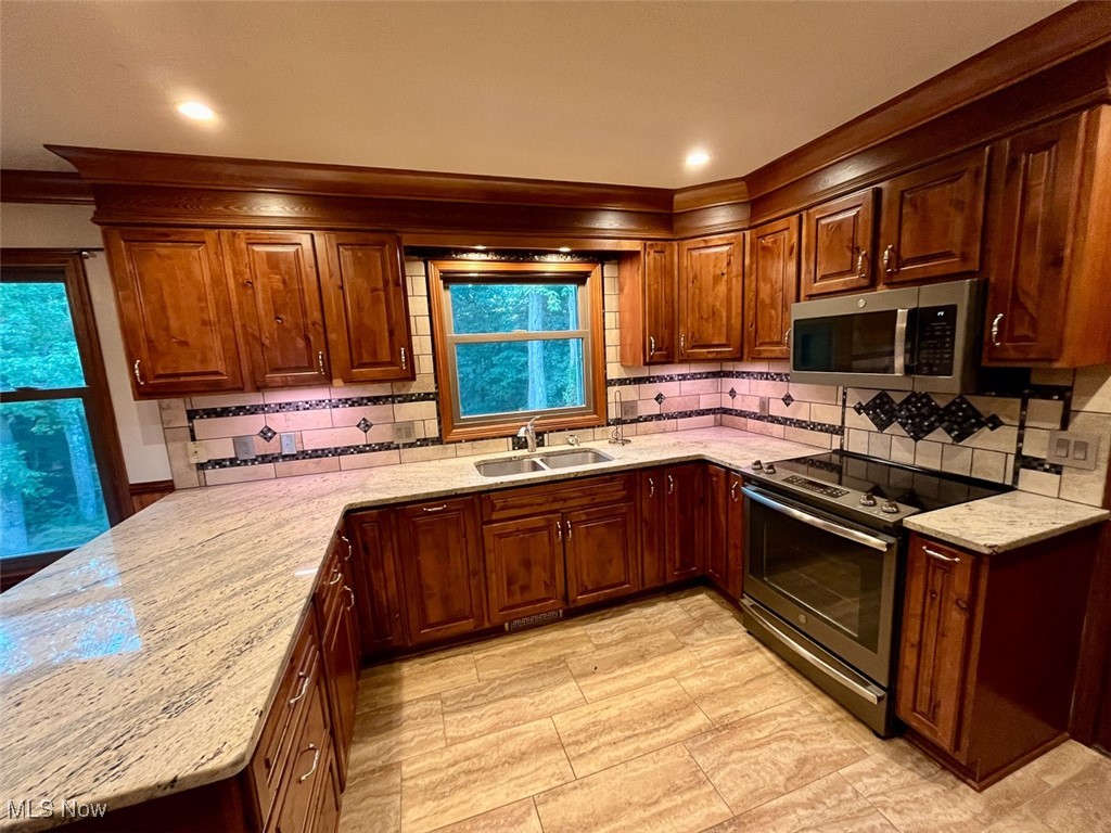 9366 Briar Road Magnolia, OH 44643 - Photo 7 of 25 Kitchen with a peninsula, appliances with stainless steel finishes, light stone countertops, backsplash, and crown molding