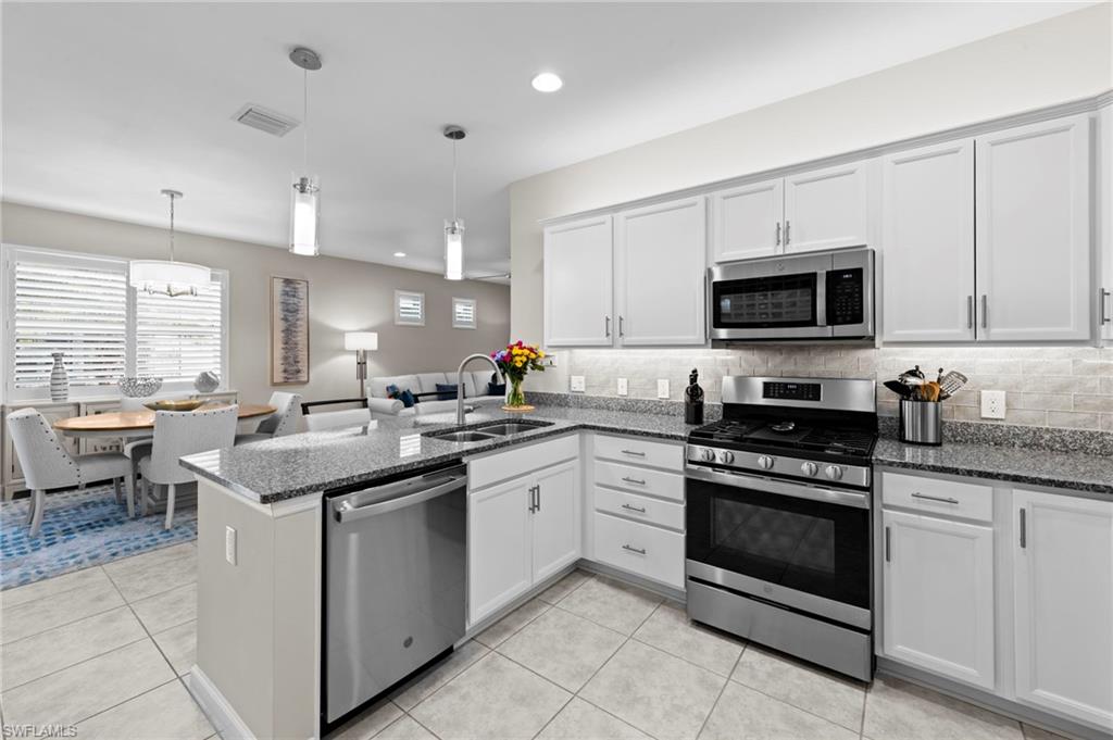 20179 Torch Key Way Estero, FL 33928 - Photo 17 of 41 a kitchen with stainless steel appliances granite countertop a stove top oven a sink dishwasher a dining table and chairs with wooden floor