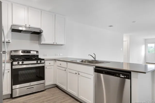 a kitchen with stainless steel appliances granite countertop white cabinets and a stove a refrigerator a sink