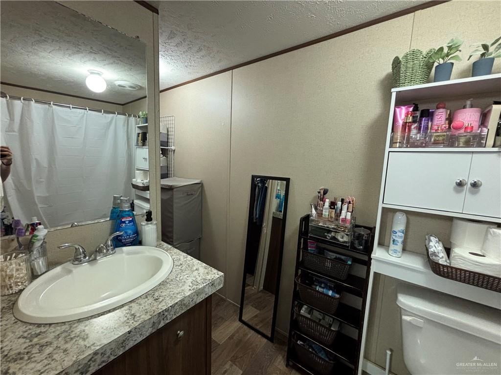 4415 Addison Drive Edinburg, TX 78542 - Photo 7 of 12 Bathroom featuring a textured ceiling, vanity, wood finished floors, crown molding, and curtained shower