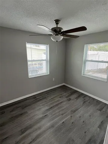 an empty room with wooden floor fan and windows