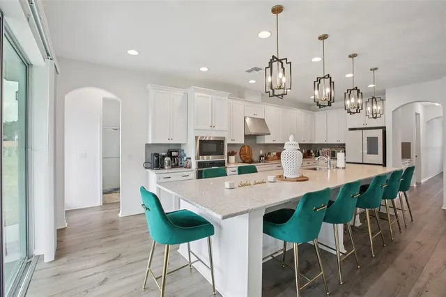 a kitchen with stainless steel appliances kitchen island granite countertop a dining table chairs and a refrigerator