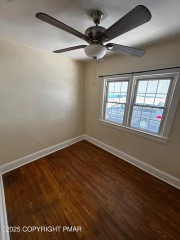 an empty room with wooden floor fan and windows
