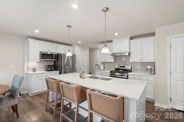 a kitchen with stainless steel appliances kitchen island granite countertop a sink a stove a refrigerator and white cabinets with wooden floor