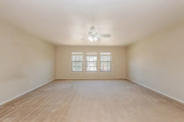 an empty room with chandelier fan and windows
