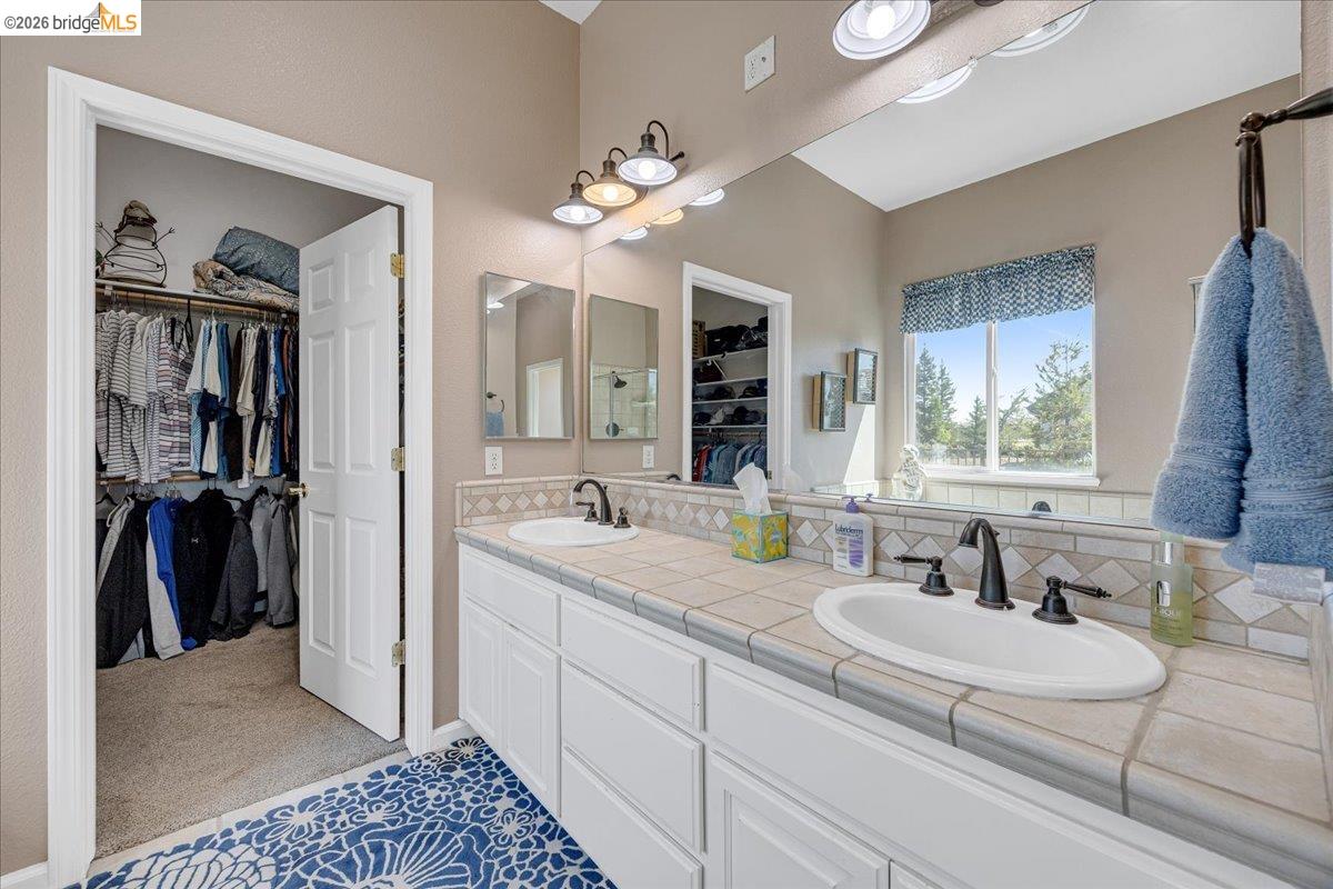158 Rock Ridge Lane Copperopolis, CA 95228 - Photo 38 of 72 Bathroom vanity featuring dual sinks with matte black fixtures, a tiled countertop, and ample storage cabinetry
