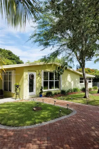 a view of a white house with a small yard plants and palm trees