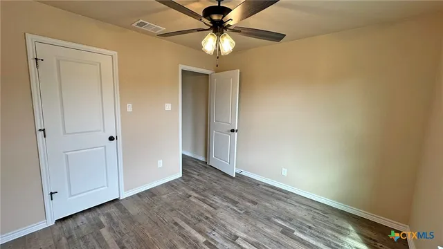 a view of empty room with wooden floor and fan