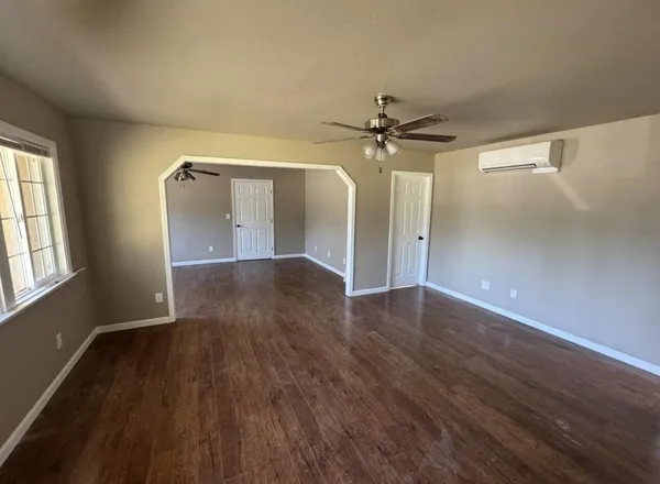 an empty room with wooden floor ceiling fan and windows