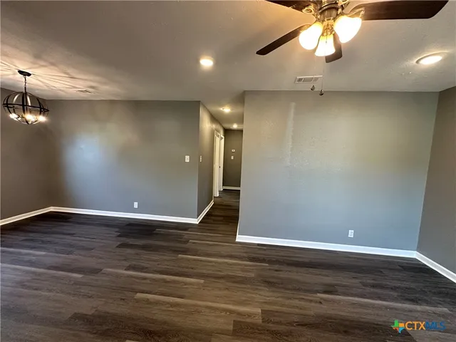 an empty room with wooden floor chandelier fan and windows