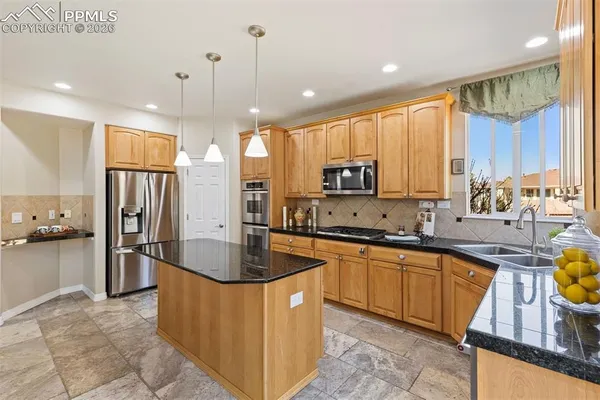 a kitchen with stainless steel appliances granite countertop a refrigerator a sink dishwasher a oven and a dining table with wooden floor